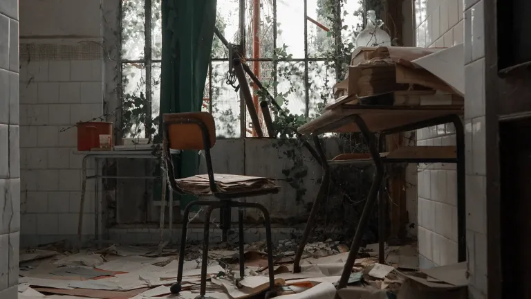God provides hope for those whose lives are buried in clutter. a desk and chair in a deteriorated room with the floor covered in old papers
