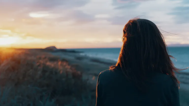No matter what trauma we have gone through, no matter who has hurt us, God can heal us through His way of life. a woman standing with her back turned as she faces the sunset on the horizon
