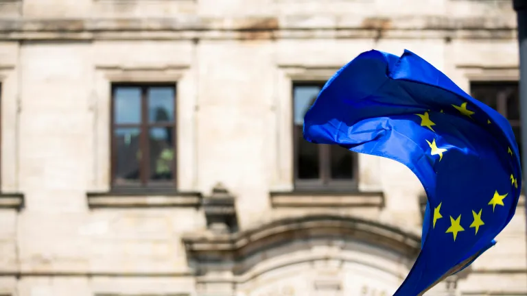 The European Union faces powerful winds of change—its future shaping rapidly as history, politics, and prophecy converge. A European Flag blowing in the wind outside of an old building.