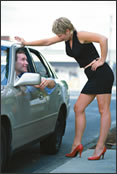 A man talking to a prostitute outside of his car.