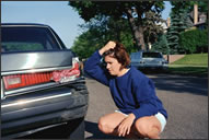Teenage girl stares in grief at broken tail light of a car.
