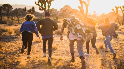 a group of young adults running towards a brown landscape with trees silhouetted in the distance