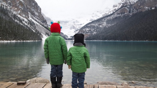Two young boys look out over the water surrounded by mountains.
