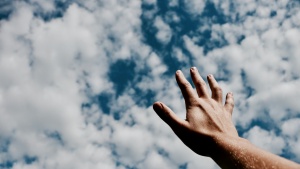 a hand reaching towards a cloudy sky