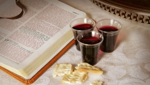 An open Bible with small cup of wine and unleavened bread.