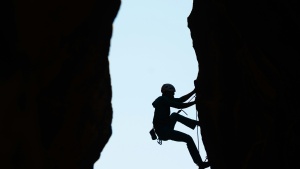 a silhouette of a woman climbing a rockface with another rockface behind her