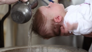 A young baby being baptized with water pouring over the child's head.