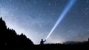 A person shining a flashlight up into the night sky.