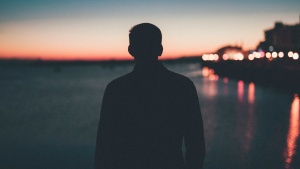 A silhouette of young man looking out over a body of water.