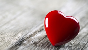 A round red heart laying on wood table.