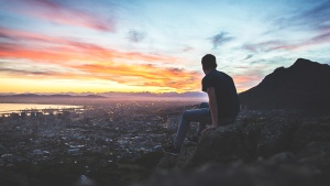 A young man sitting on a rock looking at the cityscape below.