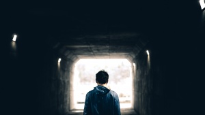 A man walking in a dark tunnel with light at the very end.