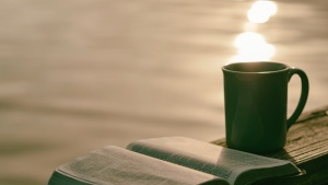 A Bible sitting on a table with a mug.