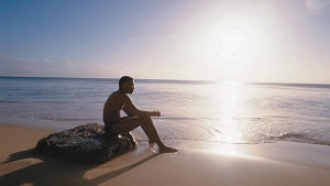 A man sitting on a rock on the beach.