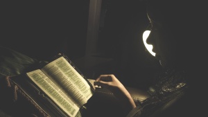 A person reading a Bible by a lamp.