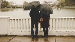 A couple standing on a bridge with umbrellas