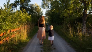 A woman and a child walking outdoors on a path through the trees