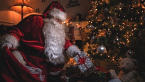 Santa Claus putting gifts under a Christmas tree.