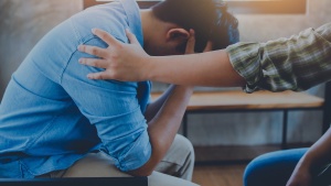 a man sitting with his head in his hands and another person with a hand on his shoulder