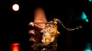 An extended hand holding a beer glass with liquid splashing over the side