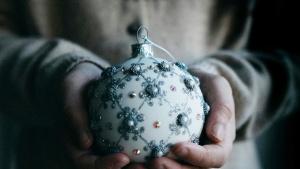 a woman holding a christmas ornament and wearing a seasonal sweater