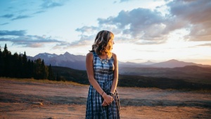 a woman wearing a long dress looking towards the sunset and she stands outside in a field