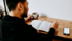 A man reading a Bible with his phone nearby.