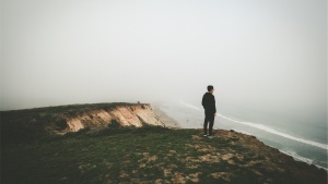 A man looking over a cliff toward the ocean.