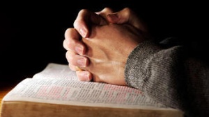 Hands folded on top of a Bible.