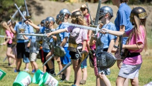 a group of children wearing pretend armor and holding plastic swords standing outdoors