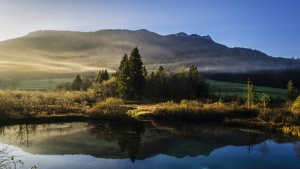 a lake with green trees by the shore and mountains in the background