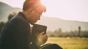 a man sitting outdoors praying while holding Bible