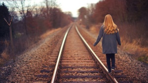 a woman walking beside a train track amidst autumn colors