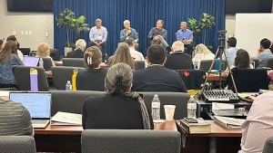 a group of people seated indoors facing four men on a stage