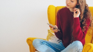 A teenager sitting in a yellow chair holding her phone