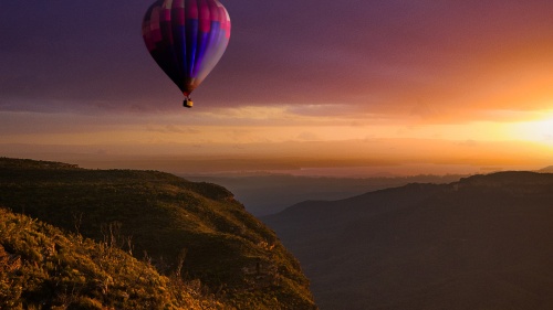 a hot air balloon flying over a hilly landscape at sunset