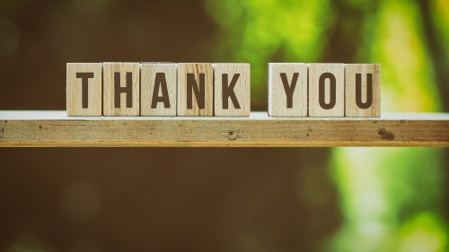 blocks spelling "thank you" balanced on a ledge against a backdrop of trees