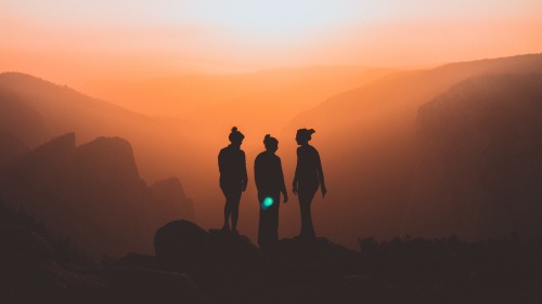 the silhouettes of three women against a backdrop of mountains at sunset.