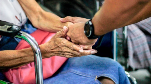 a hand reaching for the hands of an elderly person sitting in a wheelchair