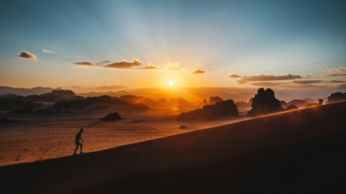 a man walking up a large hill with a sunset in the background