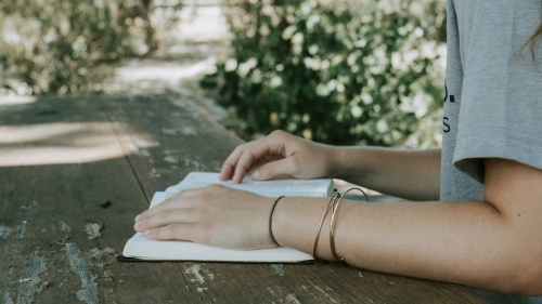 a woman's arm holding an open Bible on a table outside