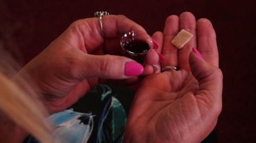 a pair of hands holding a tiny cup of wine and a piece of unleavened bread