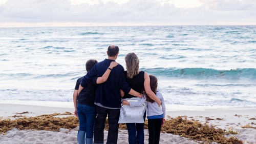 a family of four turned towards the ocean while standing on the sand