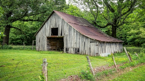 old gray barn surrounded by green grass and green trees