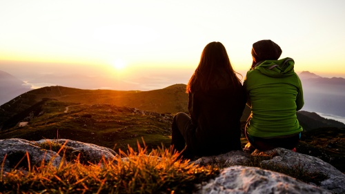 two women seated and silhouetted against the sunset with mountains in the distance