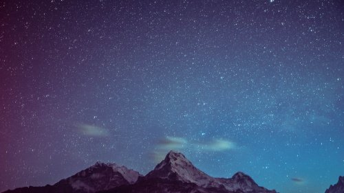 Stars in a night sky with mountain peaks in the foreground. 