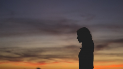 The silhouette of a young woman with the sun setting in the background.