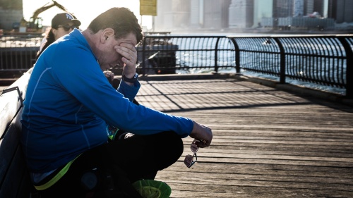 A man sitting outside with his hand on his head.