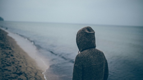 A person wearing a hoodie looking at the waves of the ocean.