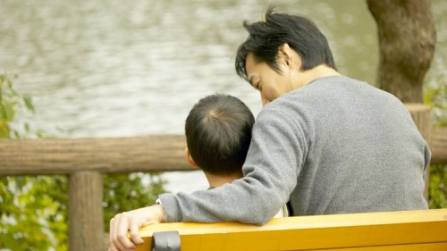 A father and son sitting together on a park bench.
